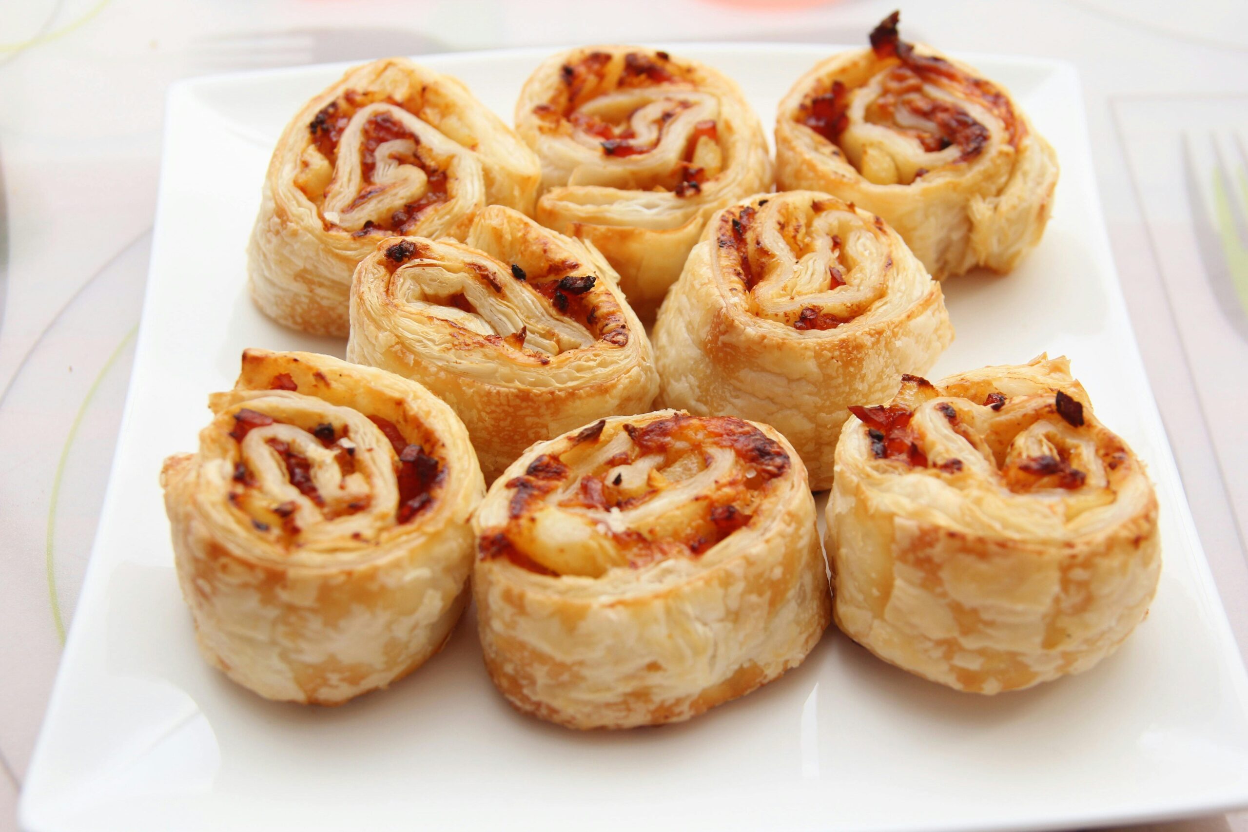 Tasty savory puff pastry rolls with cheese and bacon filling served on a white plate.