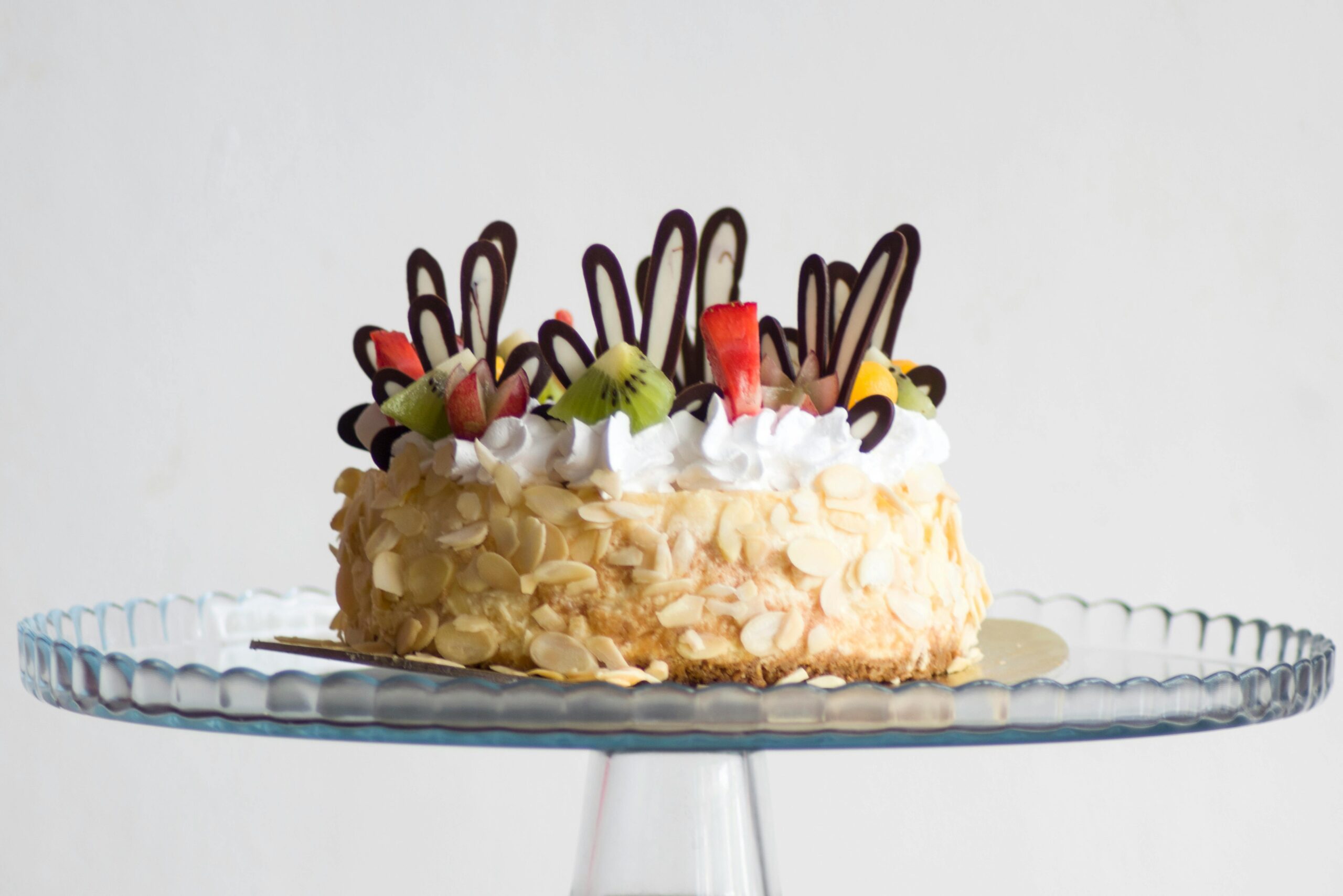 Delicious fruit-topped cake with almond slices and cream, perfect for celebrations.